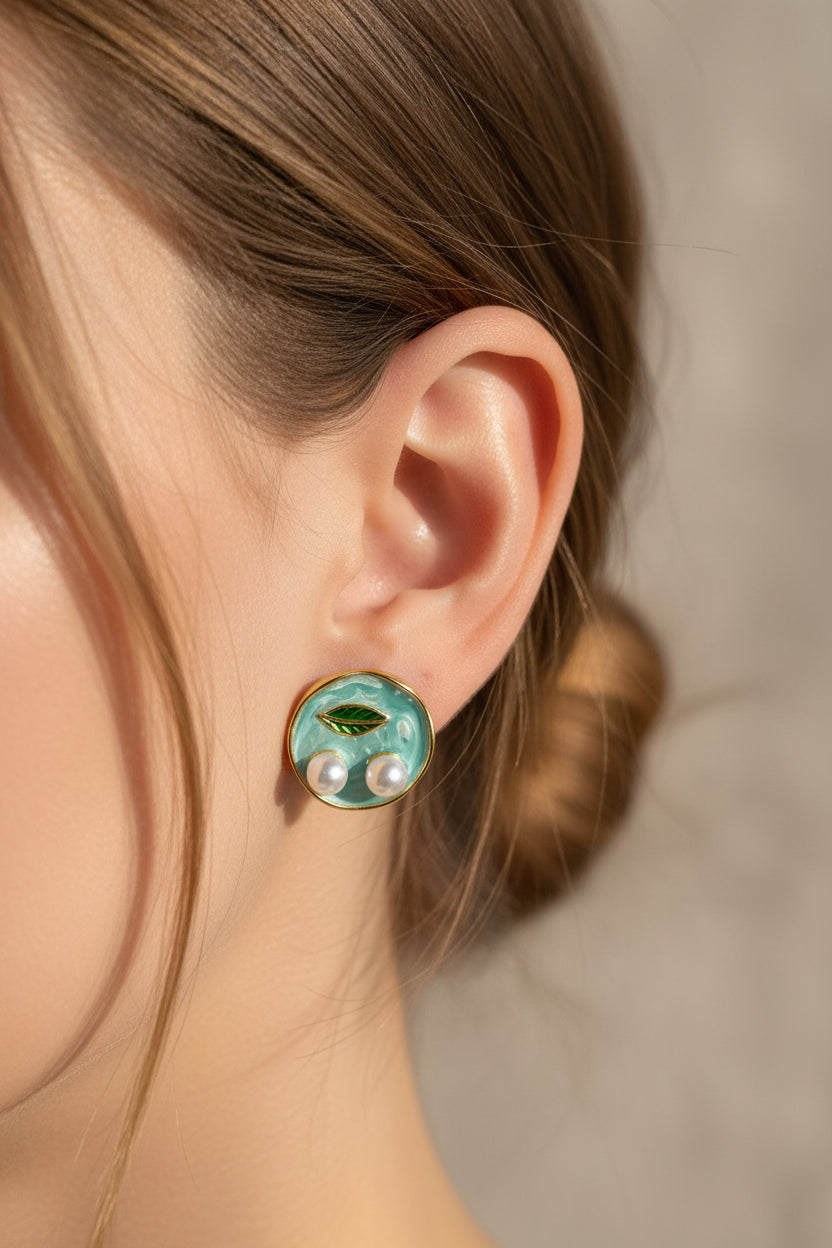 Pair of earrings with green leaves and pearls on a beige surface