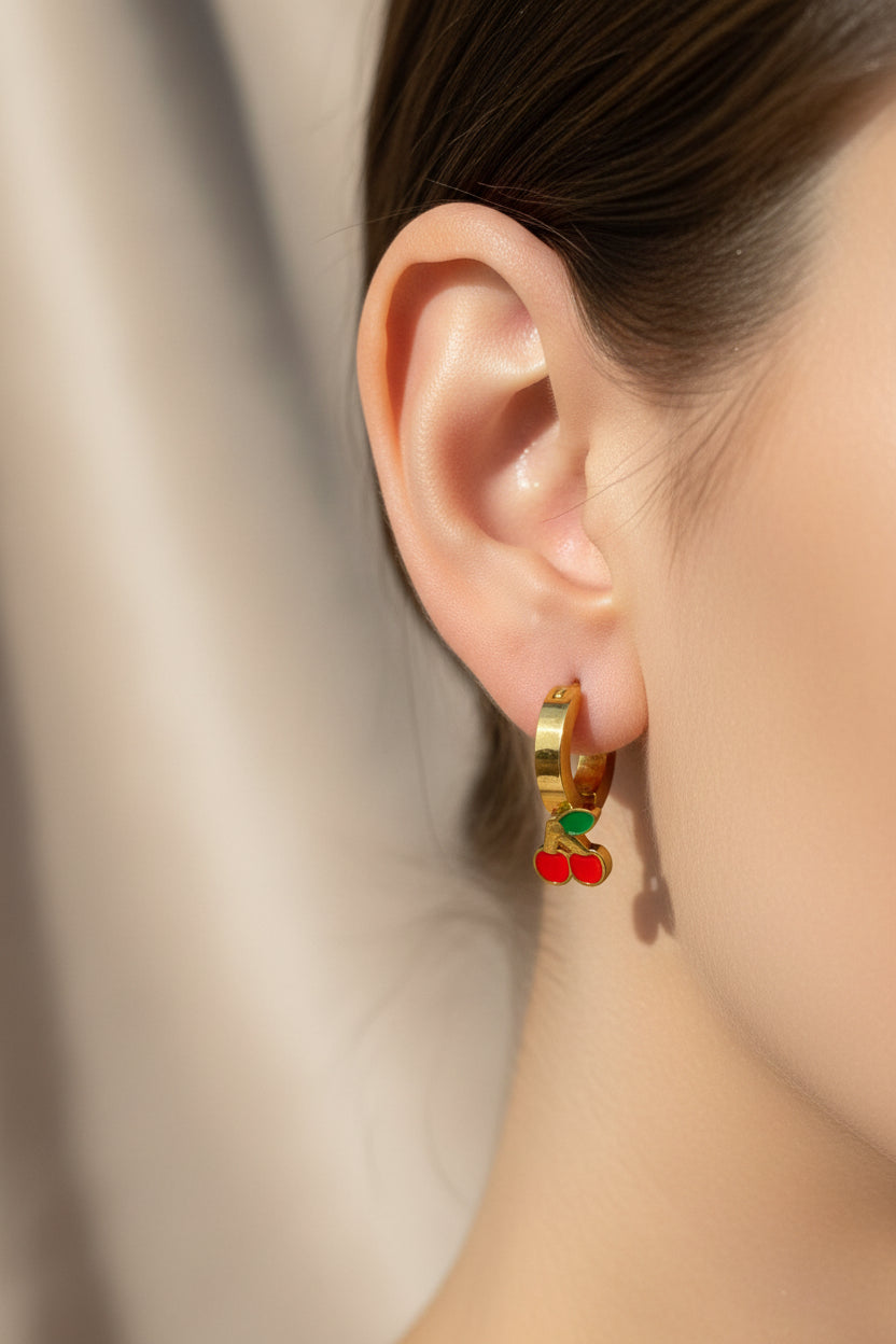 Gold earrings with red and green accents on a textured gray surface