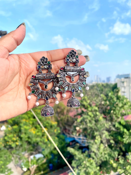 Hand holding decorative earrings with a blurred outdoor background